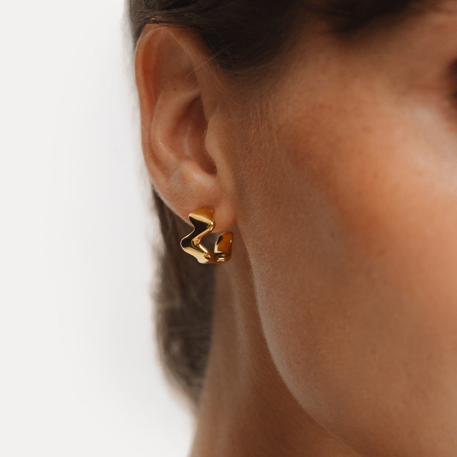 The POISE Huggie Hoops in 18k Gold Vermeil shown on the ear of a model.